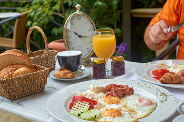 Delicious breakfast served with a cup of cappuccino. There is a clock on a table showing time 10.15 am