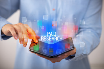 Young man holding a foldable smartphone with PAID RESEARCH inscription, educational concept