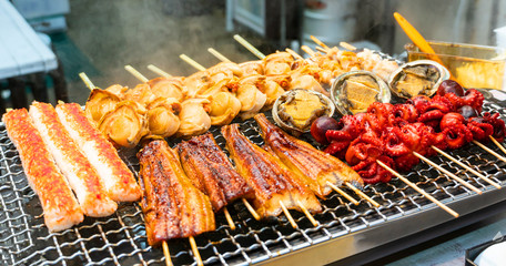 Fototapeta premium grilled seafood on roaster with smoke, japanese street food at Kuromon Ichiba Market, Japan.