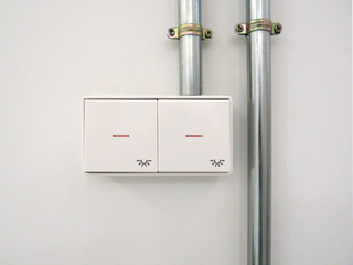 Light switches on white wall and metal tubes. Industrial and modern design.