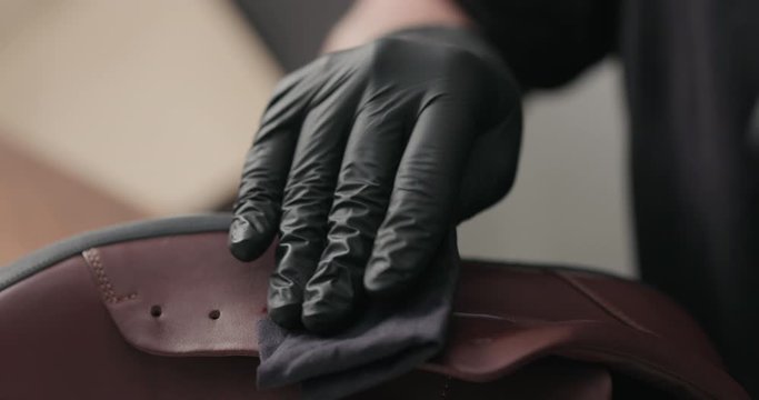 Slow motion man hands in black gloves applying protective cream to brown leather sneakers