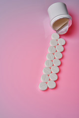 White round tablets scattered near plastic bottle of pills on pink background.