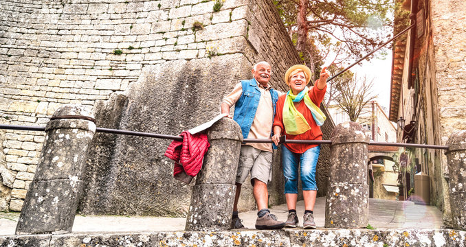 Senior Retired Couple Having Genuine Fun In San Marino Old Town Castle - Active Elderly And Travel Lifestyle Concept With Mature People At Italian Roadtrip - Warm Bright Filter With Soft Sunshine Halo