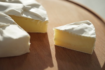Camembert cheese slice and whole on a round wooden board. Side view