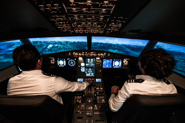 Two pilots during the flight. They are changing commands in the cockpit.  The plane is about to fly over the mountains - obrazy, fototapety, plakaty