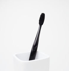 One black toothbrush, for oral care, in a white toothbrush holder on a white background