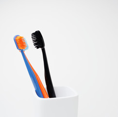 Three toothbrushes, black, blue and orange, for oral care, in a white toothbrush holder on a white background