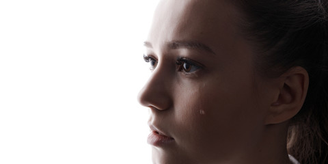 Fototapeta premium Beautiful young woman with sad big eyes crying. White background. Free space for text. Tear on cheek of unhappy female.
