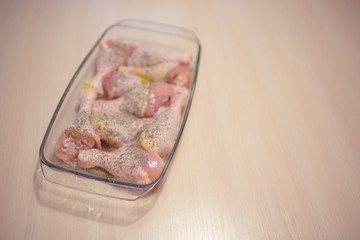 Raw chicken legs in a glass baking dish on a milk wooden table.