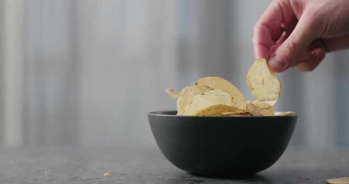 Slow motion man hand take potato chips with plack pepper from black bowl on concrtete countertop
