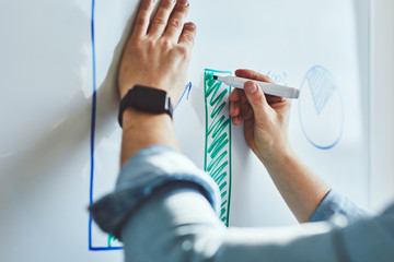 Man draws graph with marker on white board at office
