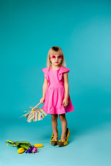 child girl blonde smiling in sunglasses in a pink dress holding a windmill on a blue background of isolate. the concept of the summer, space for text