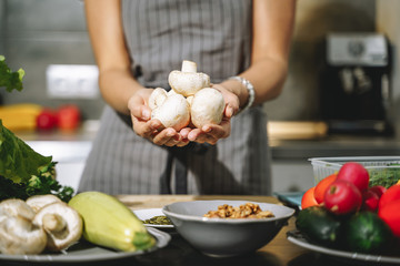 Close up of female hands holding champignon mushrooms in their hands in the kitchen