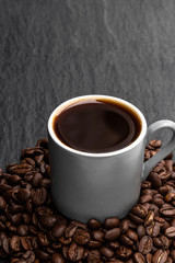 Black coffee in small cup with beans on black stone background