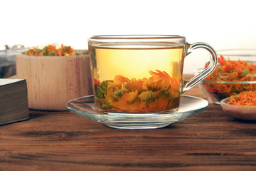 A cup of hot infusion of dried marigold flowers on a wooden table on a white background.Make up.