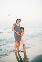 Pregnant mother and daughter enjoy together at sunet on the beach