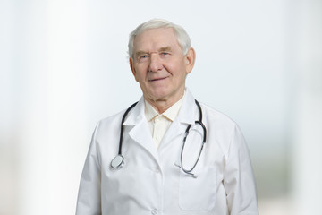 Old smiling caucasian doctor with stethoscope. Portrait of smart friendly doctor in white medical uniform. Isolated background, cutout.