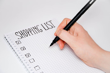 Shopping list. Hand holds a pen. Squared notebook with black pen on a white background. Record ideas, notes, plans, tasks. The list includes bread, milk,  bananas.