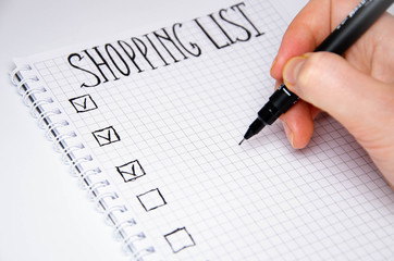 Shopping list. Hand holds a pen. Squared notebook with black pen on a white background. Record...