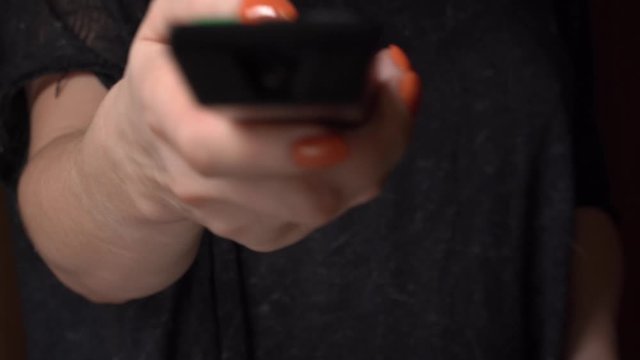 A female hand with a bright beautiful manicure switches channels on the TV remote control. We only see her hand