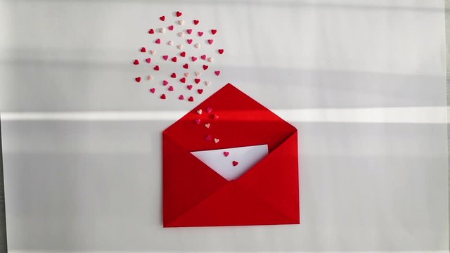 Opened red envelope and many felt hearts on white background with in the morning rays of light.Love letter mail correspondence relationship. Valentines day concept. Top view.