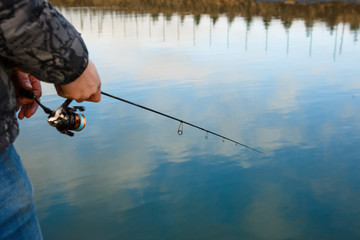 Fishing rod in the hands of a fisherman on the lake. Fisherman's hands with spinning on the background of water
