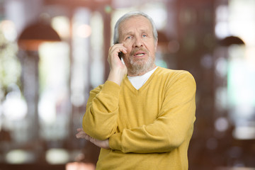 Naklejka premium Portrait of old grandfather talking on phone. Senior man in yellow wool sweater having conversation. Abstract blurred background
