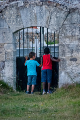 Fototapeta na wymiar White boy and black boy looking through the cemetery door