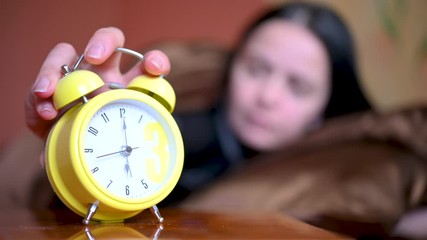 Morning. The alarm clock rings on the bedside table, the girl wakes up in bed and turns off the alarm clock and gets up. New day
