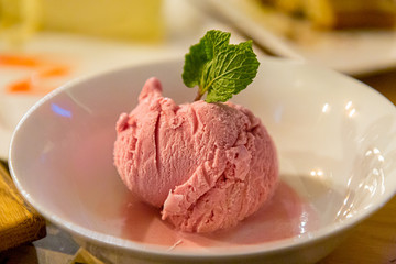 A ball of strawberry ice cream with a mint leaf is on the plate.