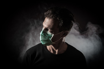 Portrait of  sick caucasian man with medical mask. Coronavirus Covid-19 concept. Black background with smoke