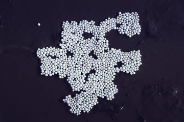 White balls of foam on wet asphalt after rain. Broken polystyrene packaging on the dark background. environmental pollution and nature