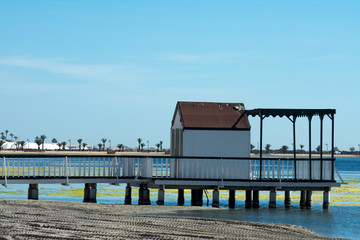A jetty at Lo Pagan on the north shore of the Mar Menor sea, in Spain.  By a beautiful beach, and promenade the wooden pier silhouettes against the calm waters of the Mediterranean.  