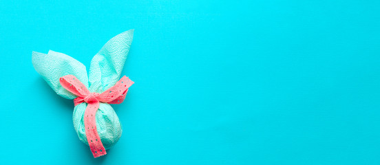 Egg gift in green paper packaging and with pink ribbon Easter Bunny wrap idea. Chocolate dragee white and gold color, multicolor colorful feathers. Minimal concept. Flat lay, Copy space, top view