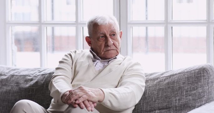 Pensive lonely older grandfather sitting alone on couch looking away