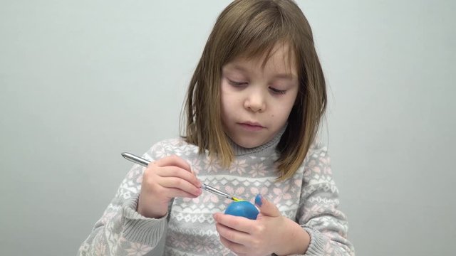 The model of European appearance is a girl of 6-7 years old. The girl is focused on coloring chicken and quail eggs for the holiday.