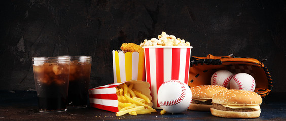 Popcorn and burger, fries and chicken nuggets on the table with softdrink cola. Baseball party food with balls for the playoffs