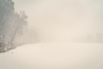 Snow blizzard over frozen river and winter forest