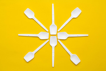 White plastic spoons on yellow background. Fast food, eco and no plastic concept. Top view. Copy, empty space for text