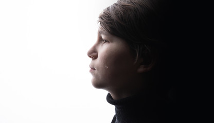 Young sad boy crying with sad eyes. White background. Free space for text. Tear on cheek of unhappy teenager.