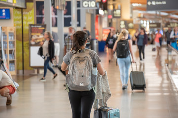 A young woman pulls her carry on luggage through an airport - obrazy, fototapety, plakaty