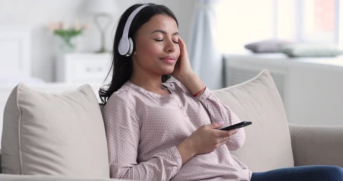 Serene relaxed african woman wearing headphones listening mobile music