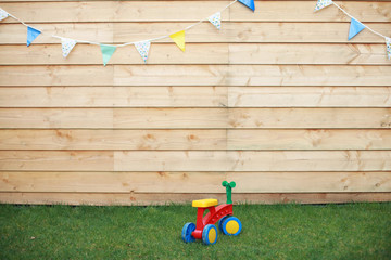 Colourful baby bicycle on a green grass with the wooden planks background with a birthday slinger flags