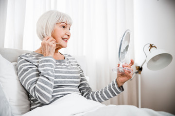 Old woman lying in bed and looking in the mirror