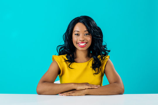 Portrait of a happy young smiling woman sitting behind desk  with arms crossed isolated on blue