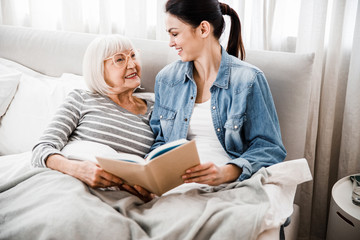 Joyful old lady reading book with adult granddaughter