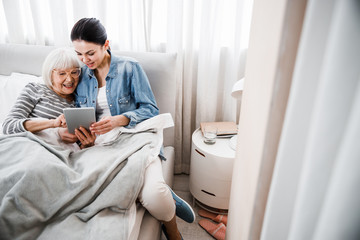Cheerful old lady and her granddaughter using modern gadget - Powered by Adobe