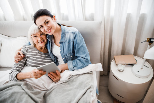 Happy Old Woman And Her Granddaughter Hugging In Bedroom