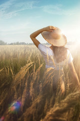 Young woman standing on a wheat field with sunrise on the background © Ruslan Shevchenko