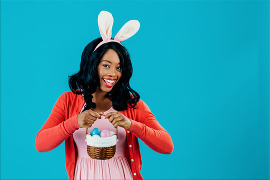 Portrait of a happy smiling mother with Easter eggs basket and bunny ears, isolated on blue background